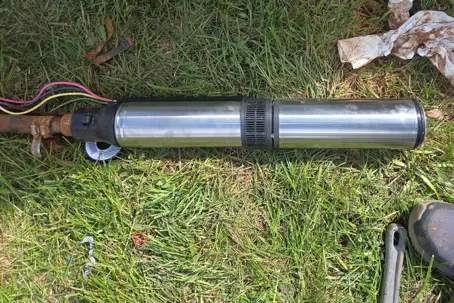 A new stainless steel submersible well pump laid out on green grass before installation.