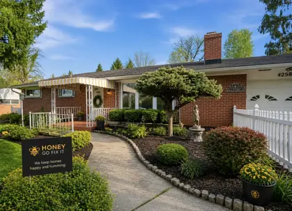 A clean, professional exterior photo of a Dayton-area brick home with a neat front yard and one subtle wet patch in the grass near the sidewalk