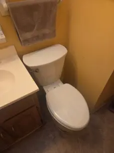 A newly installed tall elongated toilet positioned neatly next to a wooden sink vanity in a Dayton home.
