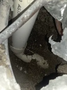 Interior excavation exposing a PVC drain line beneath a slab