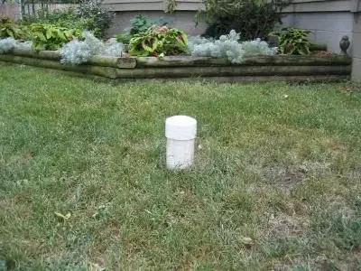 A white PVC exterior sewer cleanout pipe with a closed cap sticking up out of the grass in a residential front yard in Dayton, Ohio.