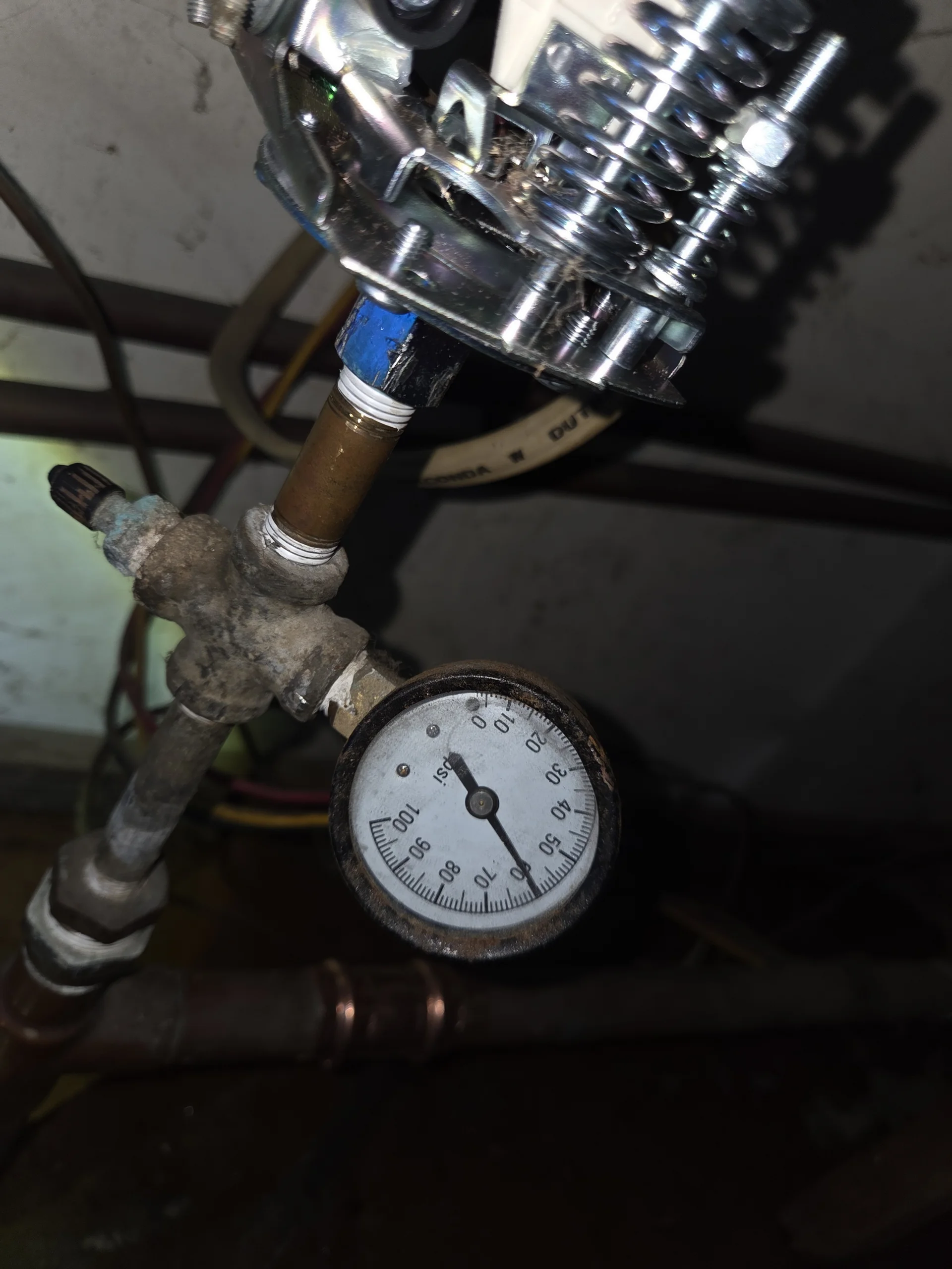 Close up view of an old rusted well water pressure gauge and corroded brass switch.