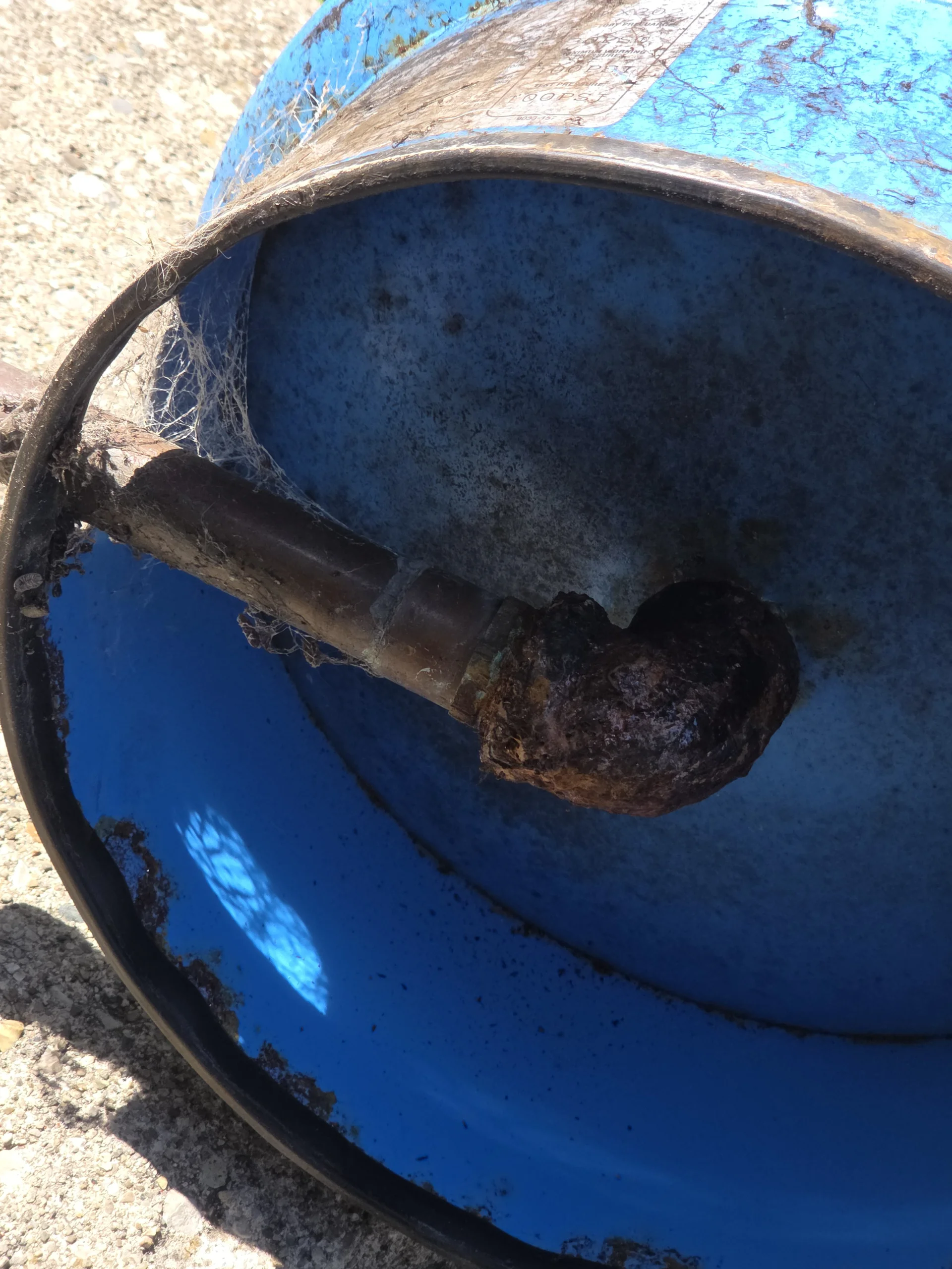 An old, worn, and rusted blue well pressure tank sitting outside on the grass.