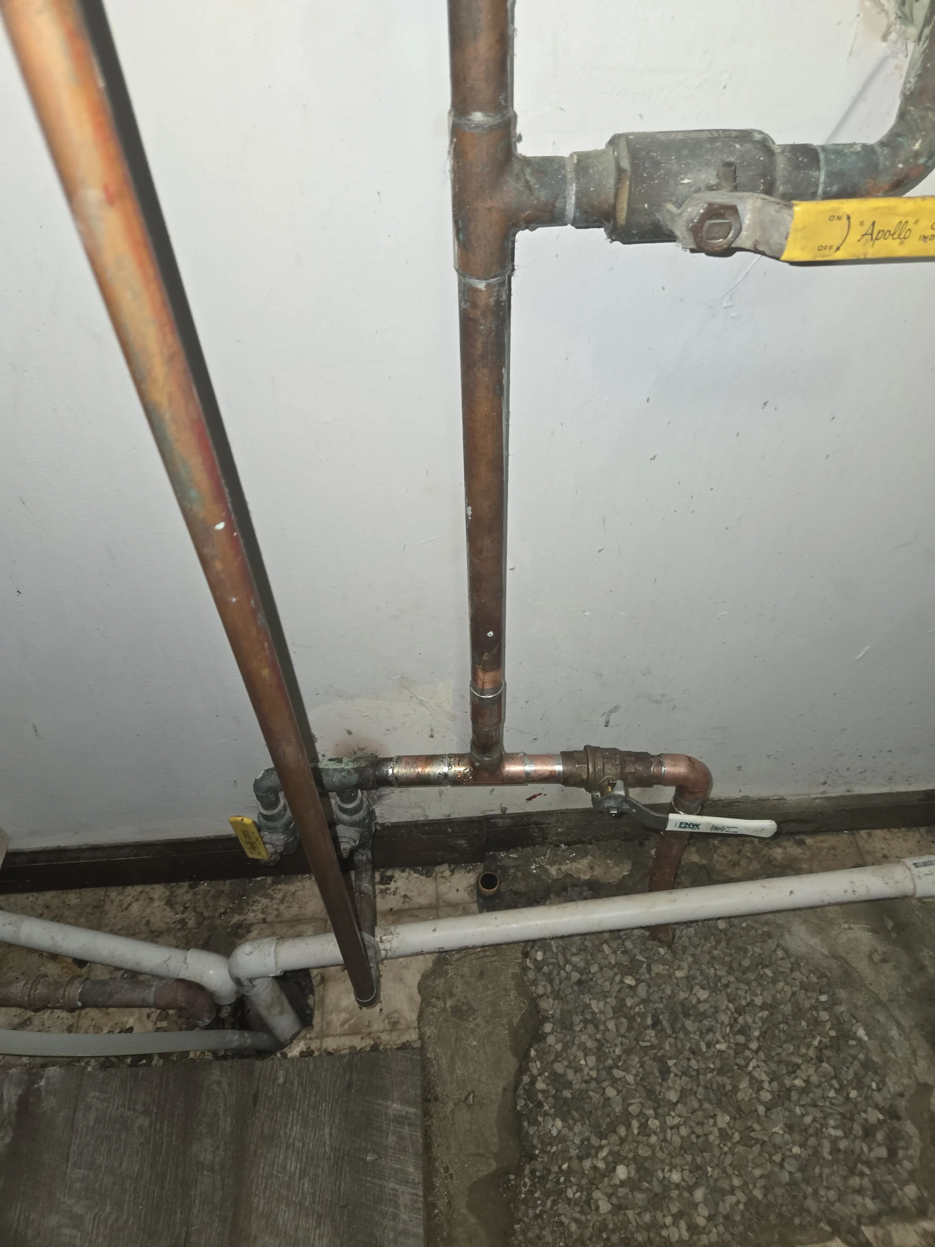 New copper water service pipes connected to valves over an open gravel section in a concrete floor.