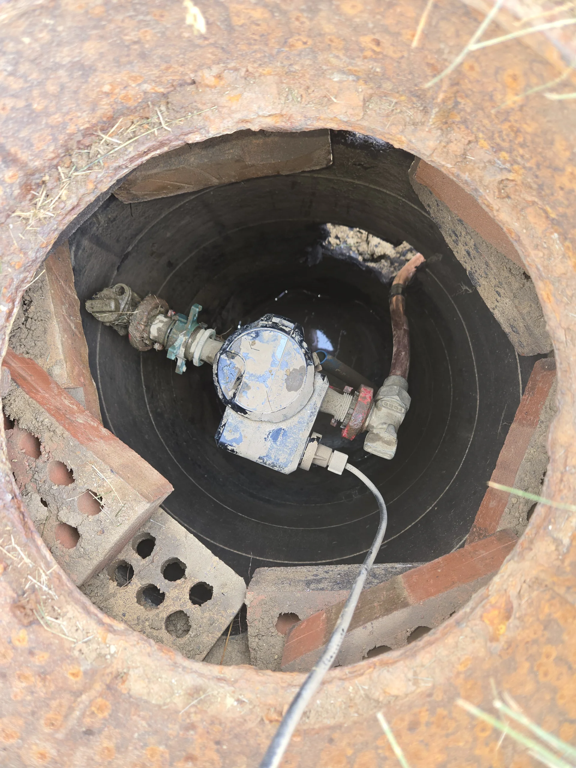 Looking down into an underground brick water meter pit assembly in a front yard.