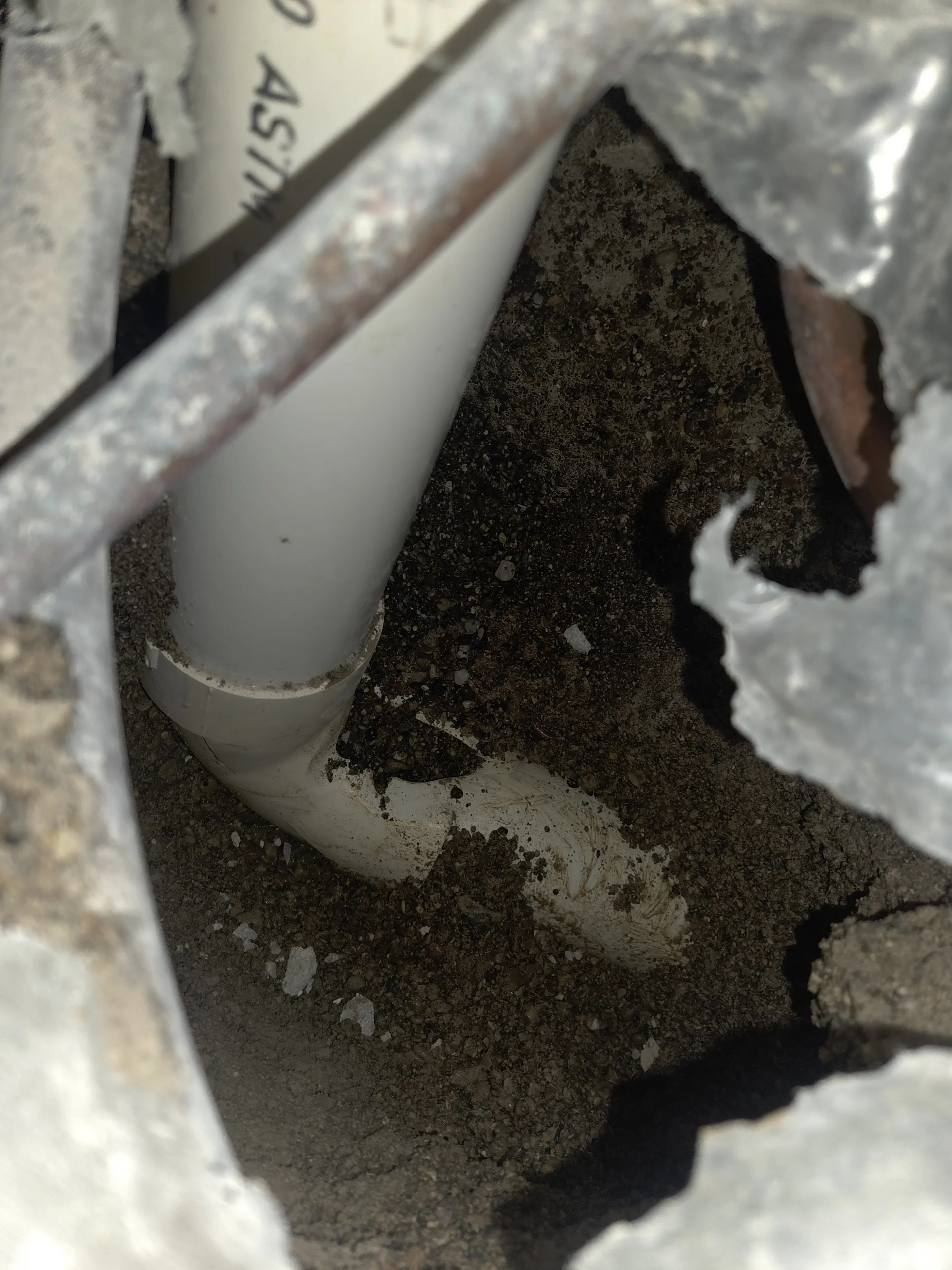 Interior excavation exposing a PVC drain line beneath a slab
